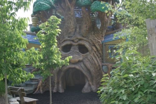 A whimsical treehouse with a face, surrounded by greenery and a play area.