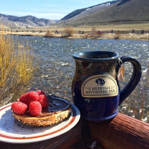 A cozy scene featuring a mug of tea and a dessert topped with raspberries, set by a scenic riverside view.