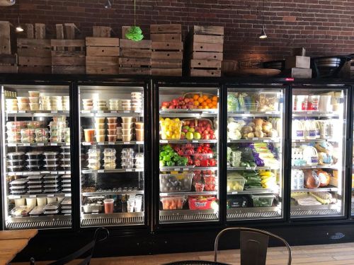 A well-stocked refrigerator display filled with various fruits, vegetables, and packaged food items in a rustic setting.