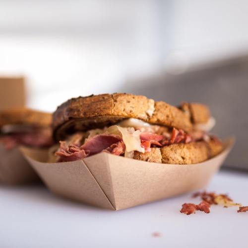 A close-up of a sandwich with layers of meat and cheese, served in a brown paper container.