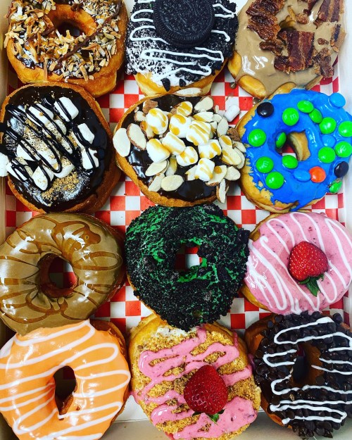 A colorful assortment of 12 donuts with various toppings, including chocolate, sprinkles, and fruit, in a box.