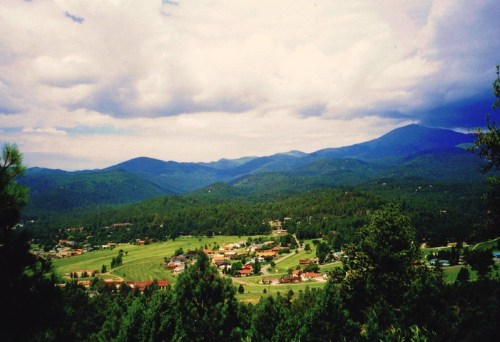 A scenic view of rolling green hills and mountains under a cloudy sky, with a small town nestled in the valley below.