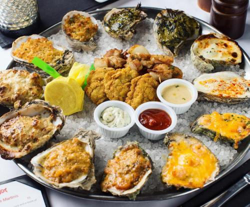 A platter of assorted oysters on ice, featuring baked, fried, and stuffed varieties, with dipping sauces and garnishes.