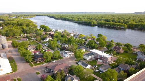 Aerial view of a small town by a river, surrounded by lush greenery and residential buildings.