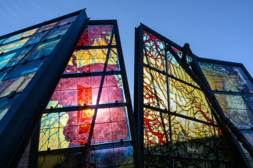 Colorful stained glass panels with intricate patterns, illuminated by sunlight against a clear blue sky.