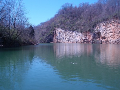 A serene lake surrounded by rocky cliffs and trees under a clear blue sky.