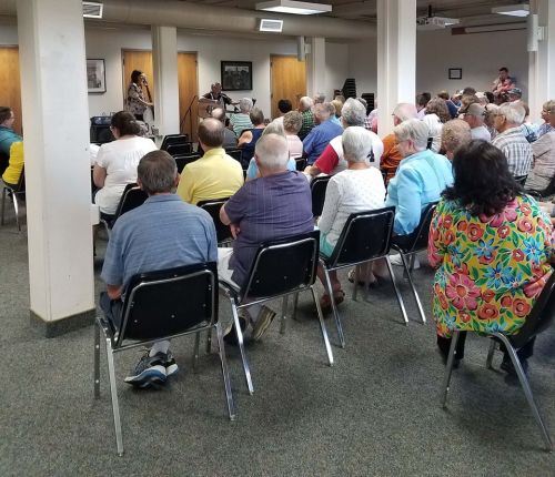 A large group of people seated in a room, listening to a speaker at the front.