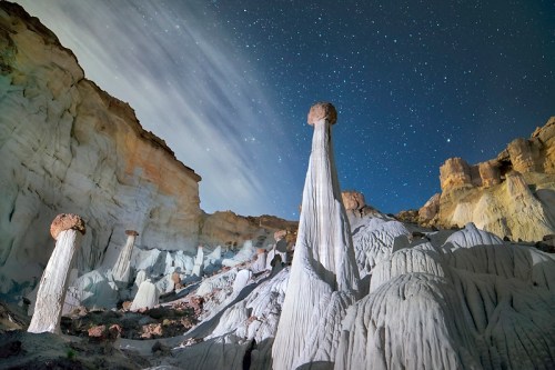 A night scene of unique rock formations under a starry sky, with clouds moving across the horizon.