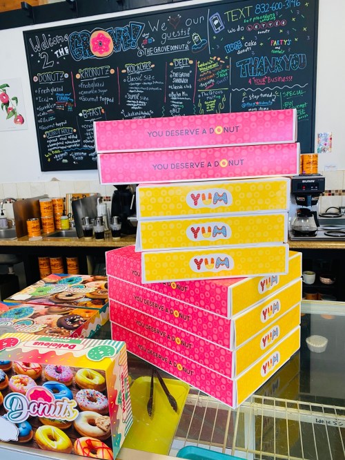 A stack of colorful donut boxes with "You Deserve a Donut" and "YUM" labels, next to a box of assorted donuts.
