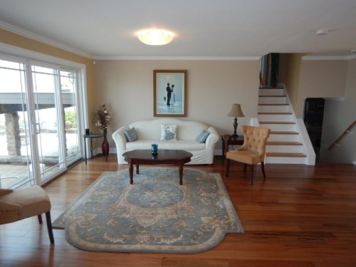 Cozy living room with a white sofa, wooden coffee table, and a patterned rug, featuring large windows and a staircase.
