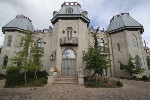 A large, ornate mansion with turreted roofs, surrounded by greenery and a stone pathway leading to the entrance.