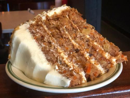 A slice of carrot cake with cream cheese frosting on a plate, showcasing layers and a textured surface.