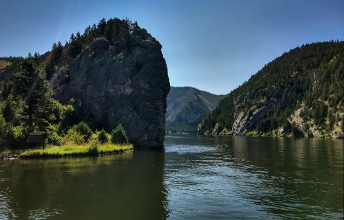 A serene river scene with rocky cliffs and lush greenery under a clear blue sky.