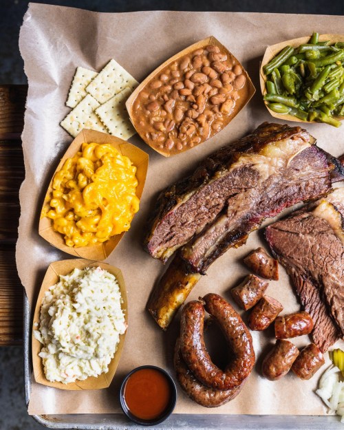 A platter of barbecue featuring brisket, sausage, macaroni and cheese, baked beans, coleslaw, green beans, and crackers.