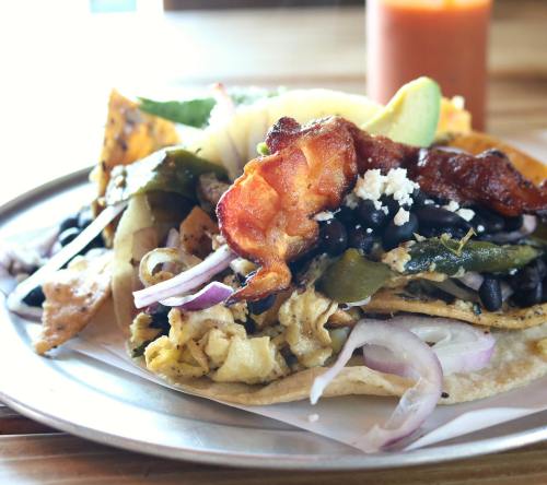 A close-up of a taco filled with scrambled eggs, bacon, black beans, onions, and peppers, served on a metal plate.