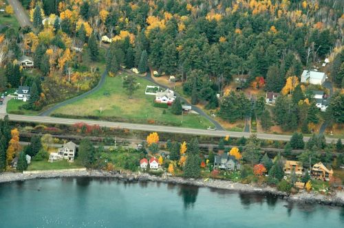 Aerial view of a colorful autumn landscape with homes, trees, and a shoreline along a calm body of water.