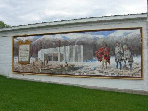 A mural depicting a historical scene with figures, a fort, and a snowy landscape, set against a cloudy sky.