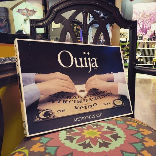 A Ouija board box featuring two hands on the planchette, resting on a colorful chair in a shop.