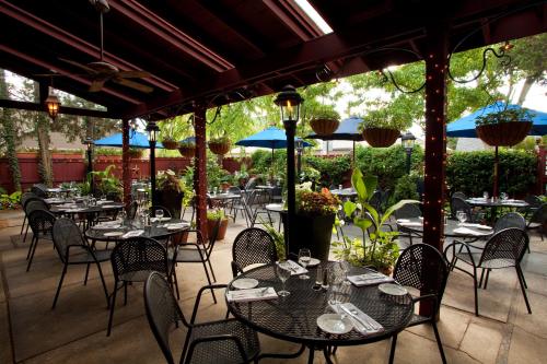 A cozy outdoor restaurant patio with black tables, chairs, and blue umbrellas surrounded by greenery.