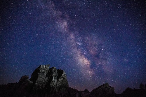 A starry night sky filled with the Milky Way, above rugged rock formations.