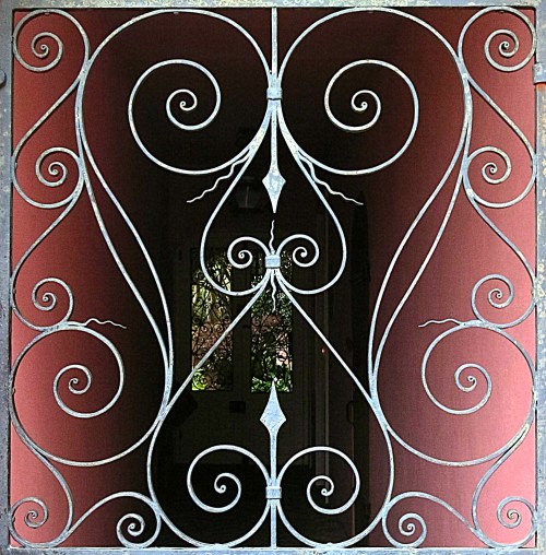 Intricate wrought iron gate with swirling patterns, framed against a red wall, revealing a glimpse of the interior.