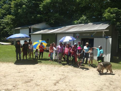 A group of people holding umbrellas stands outside a building on a sunny day, with a dog nearby.