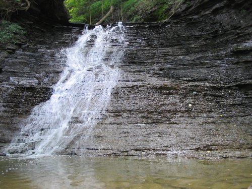 A serene waterfall cascading down a rocky cliff into a calm pool below, surrounded by lush greenery.