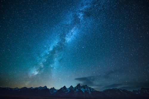 A starry night sky with the Milky Way arching over snow-capped mountains.
