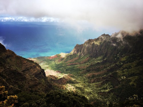 A breathtaking view of lush green mountains descending to a vibrant blue ocean under a cloudy sky.