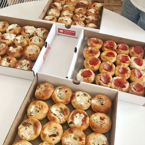 Four boxes of stuffed bread bites, some with cheese and herbs, others topped with pepperoni, arranged on a table.