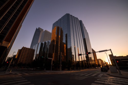 Sunset casts warm light on modern glass skyscrapers, reflecting the cityscape in a bustling urban setting.