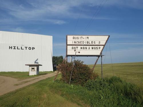 Sign for a drive-in theater showing "Incredibles 2" and "Ant-Man & Wasp" on August 17, with a grassy field nearby.