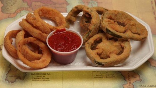 A plate of fried onion rings and jalapeño slices served with a small cup of dipping sauce.