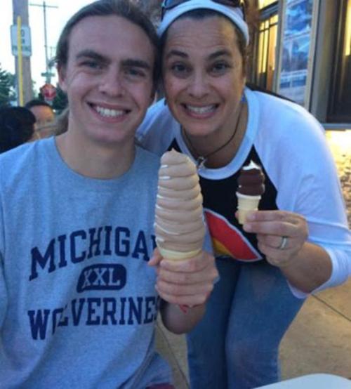 A young man and a woman smile while holding large ice cream cones outside a shop.