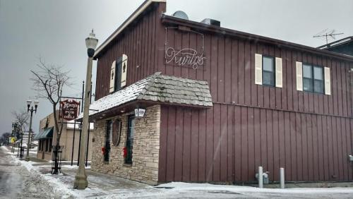 A brown wooden building with a stone entrance, decorated for winter, featuring a sign that reads "Kurt's Pub & Grill."