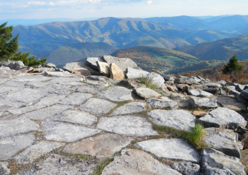 Rocky terrain with a panoramic view of rolling mountains and valleys under a clear blue sky.