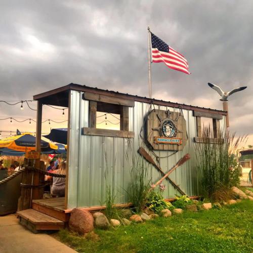 A rustic building with a metal exterior, American flag, and decorative oars, set against a cloudy sky.