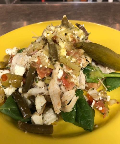 A colorful salad with shredded chicken, green beans, tomatoes, cheese, and pickles on a bed of spinach, served on a yellow plate.