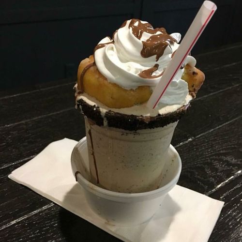 A decadent milkshake topped with whipped cream, chocolate drizzle, and a cookie, served in a cup on a napkin.