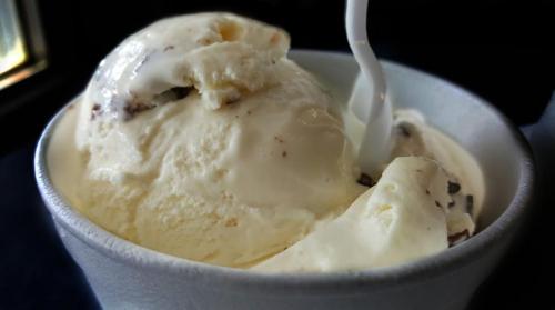 A close-up of a cup filled with creamy vanilla ice cream, featuring chocolate chip pieces and a plastic spoon.