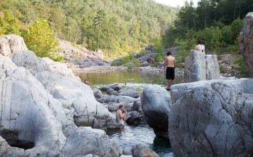 People enjoying a natural rocky river landscape, with lush greenery and calm water in the background.