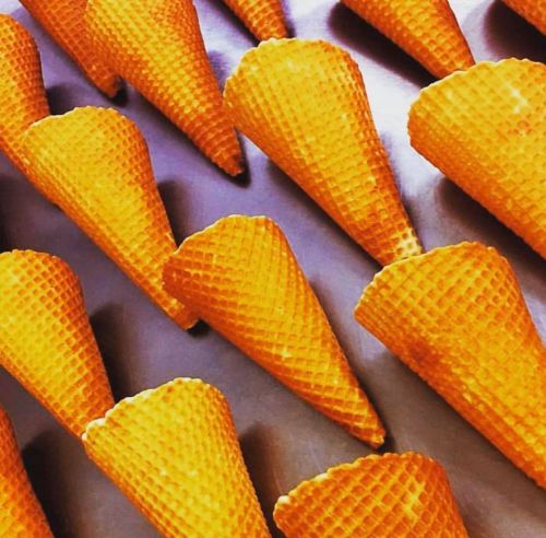 A close-up of multiple orange waffle ice cream cones arranged in a neat pattern on a surface.