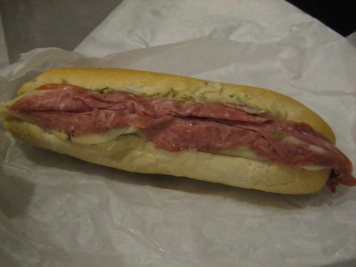 A sub sandwich filled with layers of salami and cheese, served in a soft white bread roll.