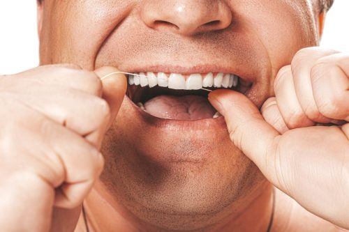 A close-up of a person using dental floss between their teeth, smiling with a focus on oral hygiene.