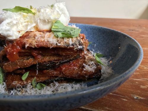 A layered dish featuring crispy eggplant, marinara sauce, cheese, and fresh herbs, served in a blue bowl.