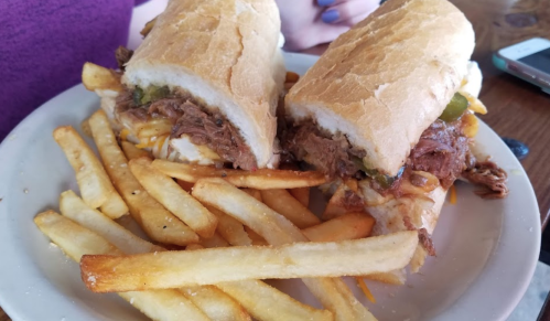 A plate with two sandwiches filled with shredded meat and jalapeños, served with a side of golden French fries.