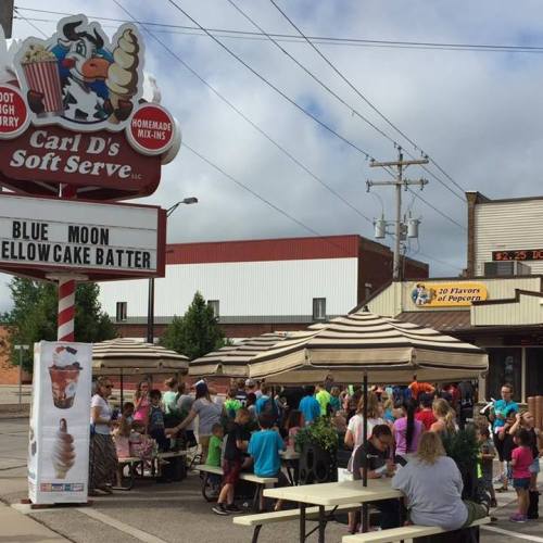 A busy outdoor ice cream shop with people enjoying treats under umbrellas on a cloudy day.
