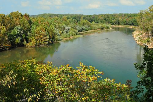 A serene river flows through a lush, green landscape with trees and a clear blue sky in the background.