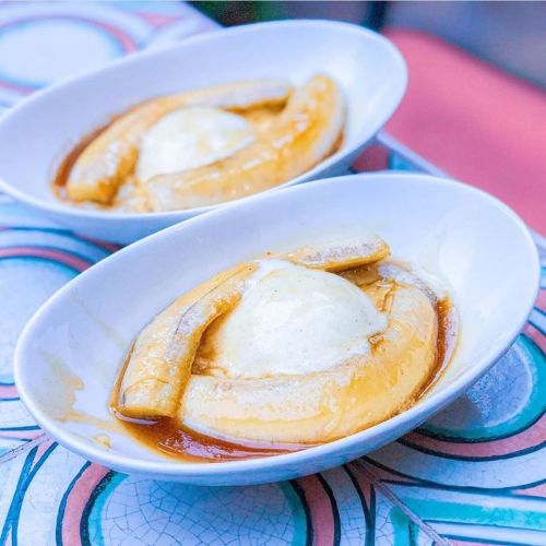 Two oval dishes with caramelized bananas and a scoop of vanilla ice cream, served on a colorful patterned table.
