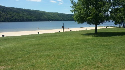 A serene beach scene with a sandy shore, calm water, and green hills in the background under a clear blue sky.